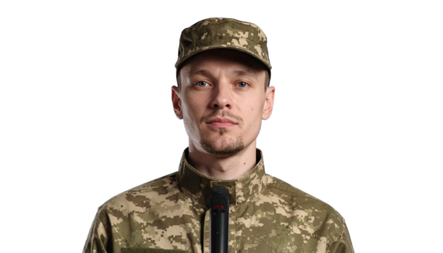 A military officer standing with a microphone, focused on duty. The officer is wearing a camouflage uniform, representing strength and dedication