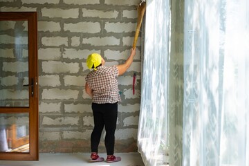 Woman with yellow cap cleaning window with broom inside under construction house with grey brick...