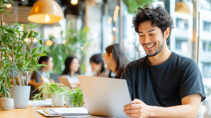 Cheerful man working remotely on laptop in modern cafe surrounded by greenery and natural light, showcasing flexibility and innovation in collaborative environment