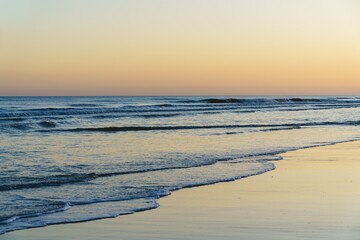 Gentle waves roll onto the beach as the sky glows softly during sunset.
