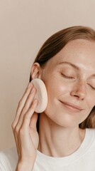 Young woman with clean skin gently using a facial sponge. Eyes closed and smiling, natural skincare, self-care routine.concept. 