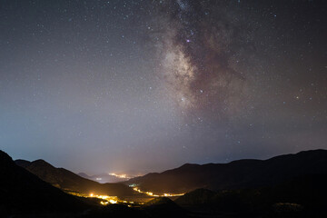 Milky Way galaxy above mountains and glowing village lights at night