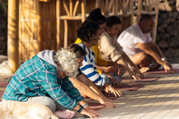 Group of people doing yoga exercises outdoors in the seated forward bend pose