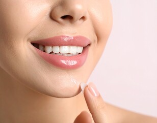 Obraz premium Close-up of a smiling woman's lips and chin as she applies a small dab of clear balm or cream to her chin with her fingertip, showcasing healthy skin and a radiant smile.