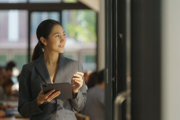 Smiling female office worker checking reports and using a digital tablet at the office.