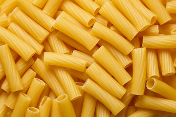 Yellow tortiglioni pasta pieces are scattered randomly on a textured surface, showcasing their...