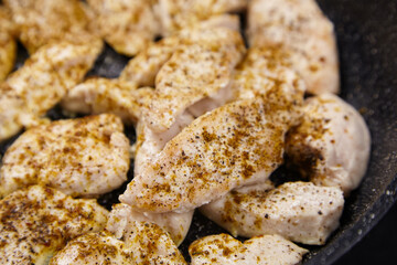 Raw chicken fillets seasoned with spices are arranged in a frying pan, showcasing the preparation...