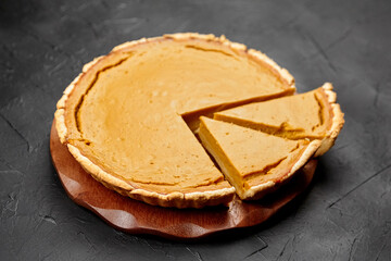 Pumpkin pie on a wooden serving board, with a slice cut out, showcasing the creamy filling and flaky crust, perfect for autumn celebrations and festive gatherings