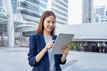 Smiling asian businesswoman holding digital tablet while standing in front of modern business...