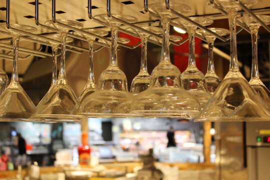 Empty martini and champagne glasses hang from a hanging rack against blurred display windows in a bar
 - Powered by Adobe