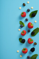 Frame of strawberries, blueberries, blackberries and mint leaves on a blue background. Space for...