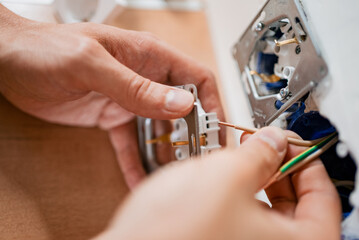 Close-up of an electrician's hands carefully connecting wires to a new electrical outlet, demonstrating the process of electrical installation in a home setting