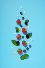 Scattered fresh berries, mint leaves, and white chocolate drops on a bright blue background. Healthy summer ingredients.