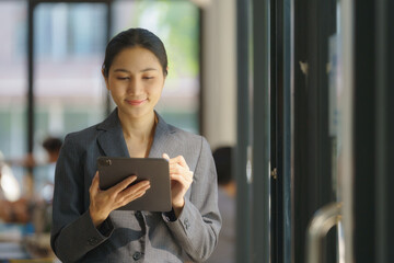 Smiling female office worker checking reports and using a digital tablet at the office.