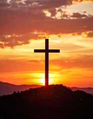 Silhouetted cross atop a hill against a vibrant, red and orange sunset sky