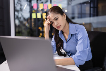 Businesswoman feeling stressed working at desk in office night time.