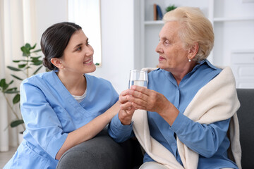 Nurse giving glass of water to senior woman indoors. Home health care service