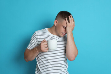 Man with cup of drink suffering from hangover on light blue background