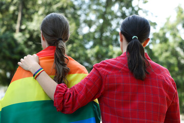 LGBT concept. Women in rainbow wristband with flag outdoors, back view