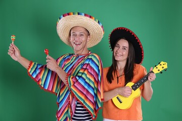 Happy couple in sombrero and Flamenco hats playing musical instruments on green background