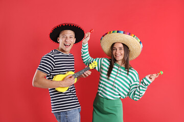 Happy couple in sombrero and Flamenco hats playing musical instruments on red background