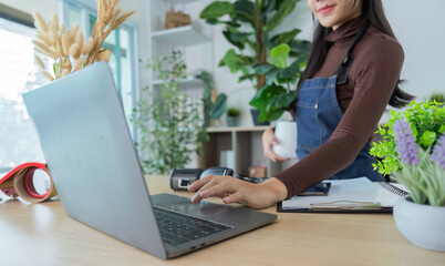 Remote Work. Young woman multitasking with laptop and coffee in a plant-filled workspace.