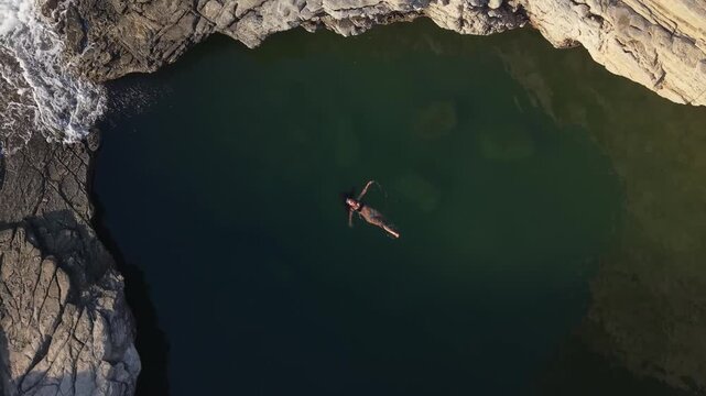 Aerial top-down footage of Giola in Thasos, capturing a woman swimming in the emerald natural pool surrounded by dramatic rocks and turquoise sea