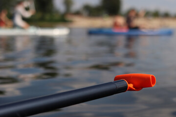 Stand-up paddleboard handle, close-up. Active way of summer recreation. Active summer vacation. Water sports. Light plastic paddle on the background of water, river
