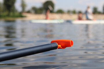 Stand-up paddleboard handle, close-up. Active way of summer recreation. Active summer vacation. Water sports. Light plastic paddle on the background of water, river