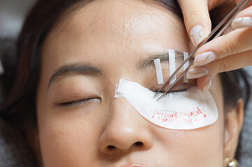 Young southeast asian woman getting relaxing eyelashes extension procedure in beauty salon. female...