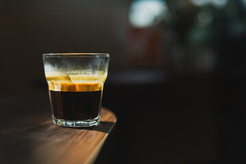 Glass of fresh double espresso on wooden table in dark background.
