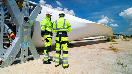 Workers inspect large wind turbine blade at construction site under bright blue sky