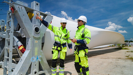 Two workers discussing wind turbine installation at a construction site under a clear blue sky