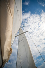 Full white sails blown by the wind against blue sky during sailing near Croatia. Symbol of movement, freedom and summer maritime journey.