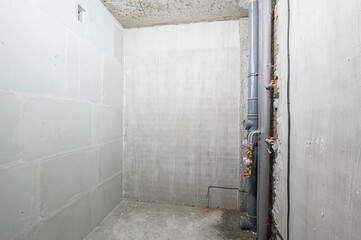 Interior shot of an unfinished room. Walls are made of gypsum blocks and concrete, pipes on the...