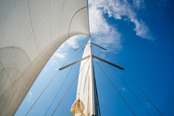 Fototapeta premium White sails filled with wind, seen from the bow of a sailing yacht near Croatia. Freedom, clean energy, adventure and mindful travel on the open sea.
