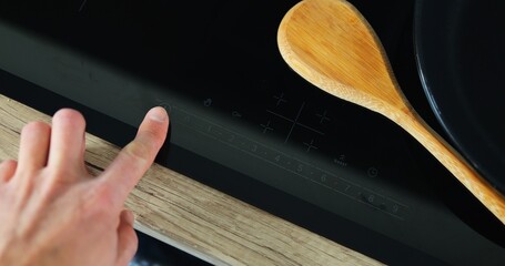 Cook presses finger on modern hob screen and turns on cooking mechanism setting mode. Man prepares...
