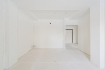 stark white, unfinished room. Bare walls, concrete floor, with a doorway to another room