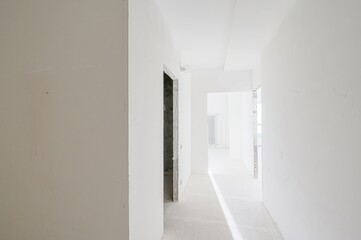 bright, narrow hallway under renovation with white walls, door openings and a bare lightbulb