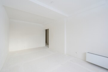 bright, empty room with all white walls and ceiling. A doorway leads to another room. The floor is also white and looks like it is covered with a protective material