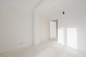 stark, white room under construction.  Bright light streams through unseen windows. An open doorway leads to another space