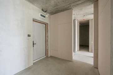 interior view of a room under construction. Concrete floors and ceilings are visible, with unfinished walls and a door wrapped in plastic