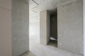 stark, gray room under construction with exposed concrete, walls, and wiring. An empty doorway is...