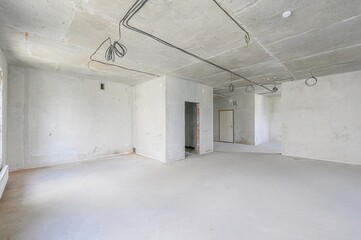 An unfinished, empty room with concrete walls and ceiling, visible wiring, and doorways. The space...