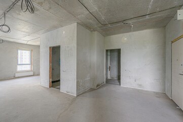 Bare, empty room under construction with concrete walls, ceiling, and floor. Electrical wires are visible