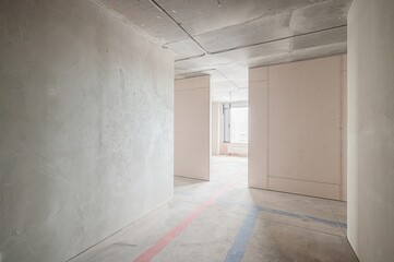 unfinished room under construction, featuring bare concrete walls, a ceiling with exposed wiring, and marked floor lines. The space is minimalist and industrial in feel