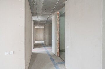 An interior shot of a hallway under construction. The walls are unfinished, and the ceiling is exposed concrete with wiring