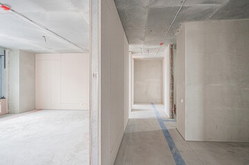 Interior shot of an unfinished, concrete space. Walls are partially constructed; exposed ceilings. A corridor leads to additional rooms