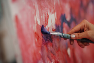 Artist painting abstract artwork with brush and red and purple colors