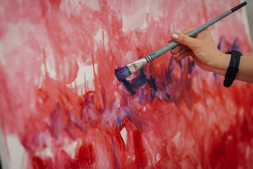 Artist painting red and purple on canvas with brush